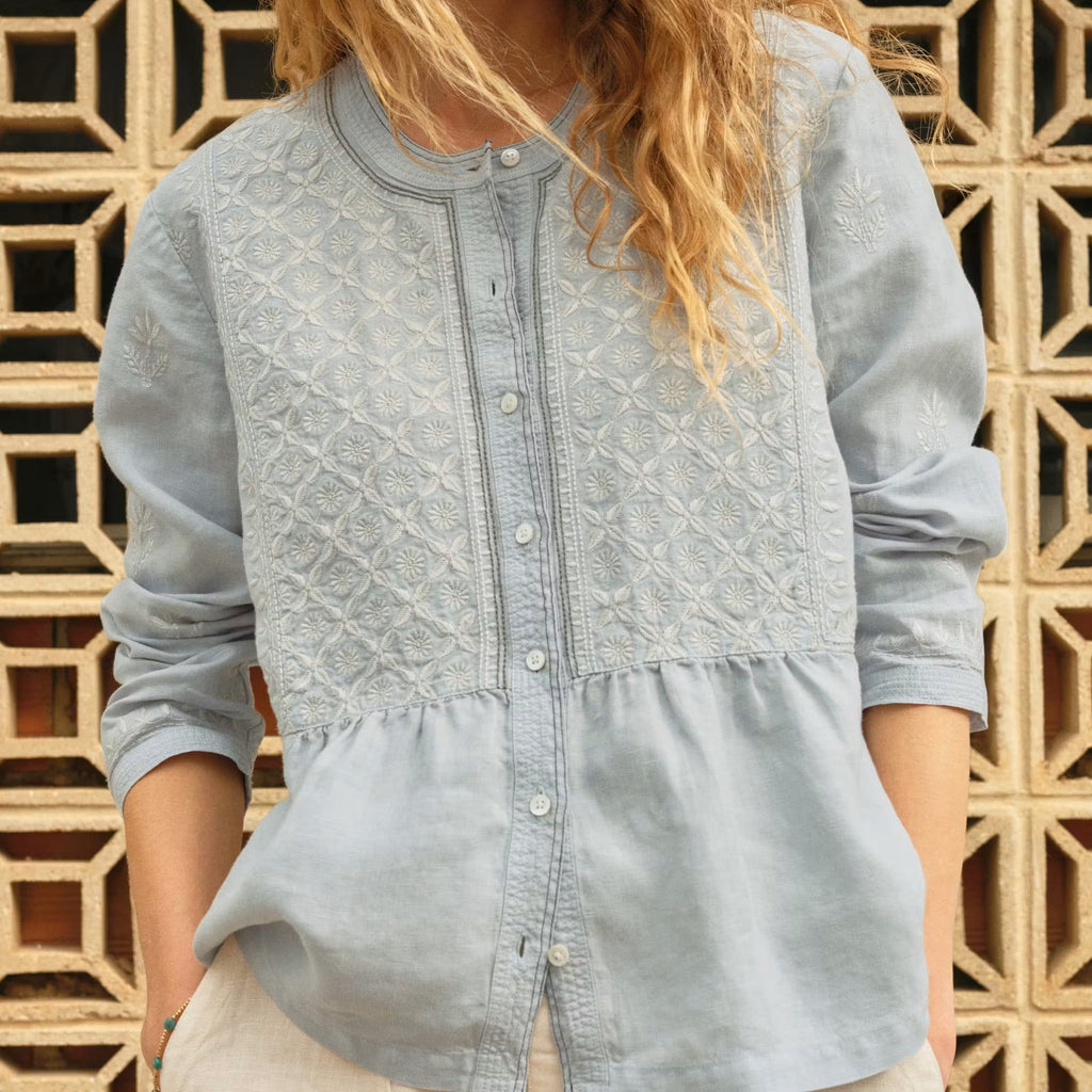 Woman wearing a light blue embroidered shirt against a geometric wooden background
