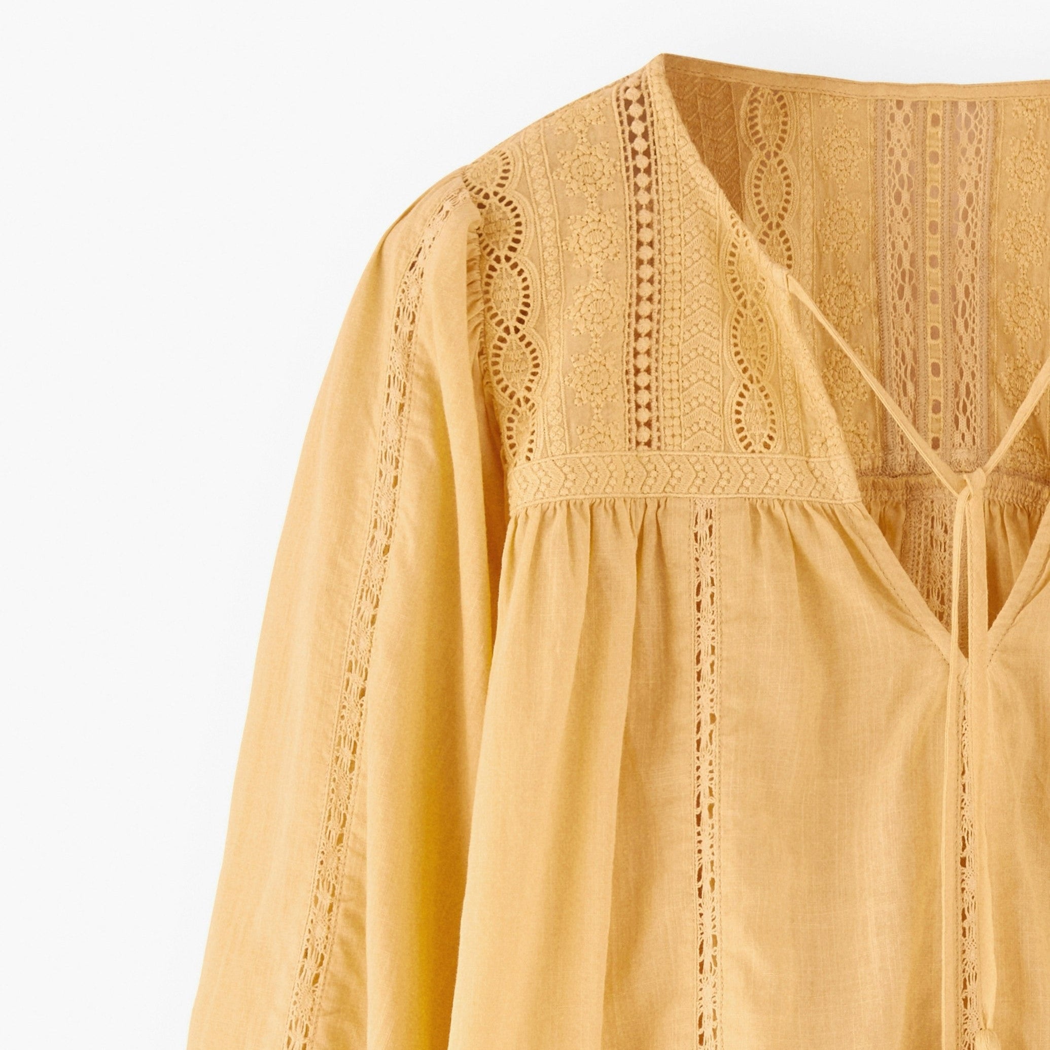 Yellow blouse with intricate lace detailing on a white background