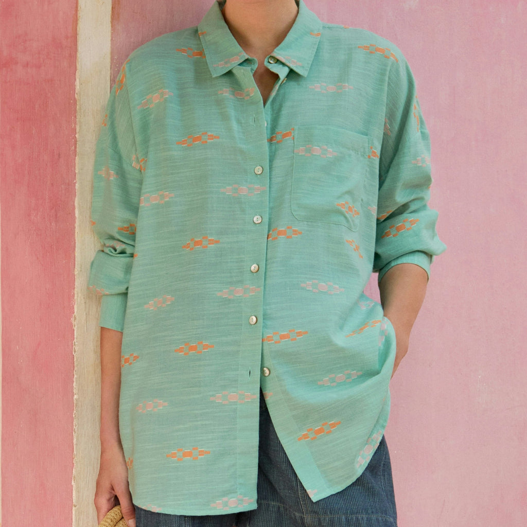 Woman wearing a teal patterned shirt against a pink wall