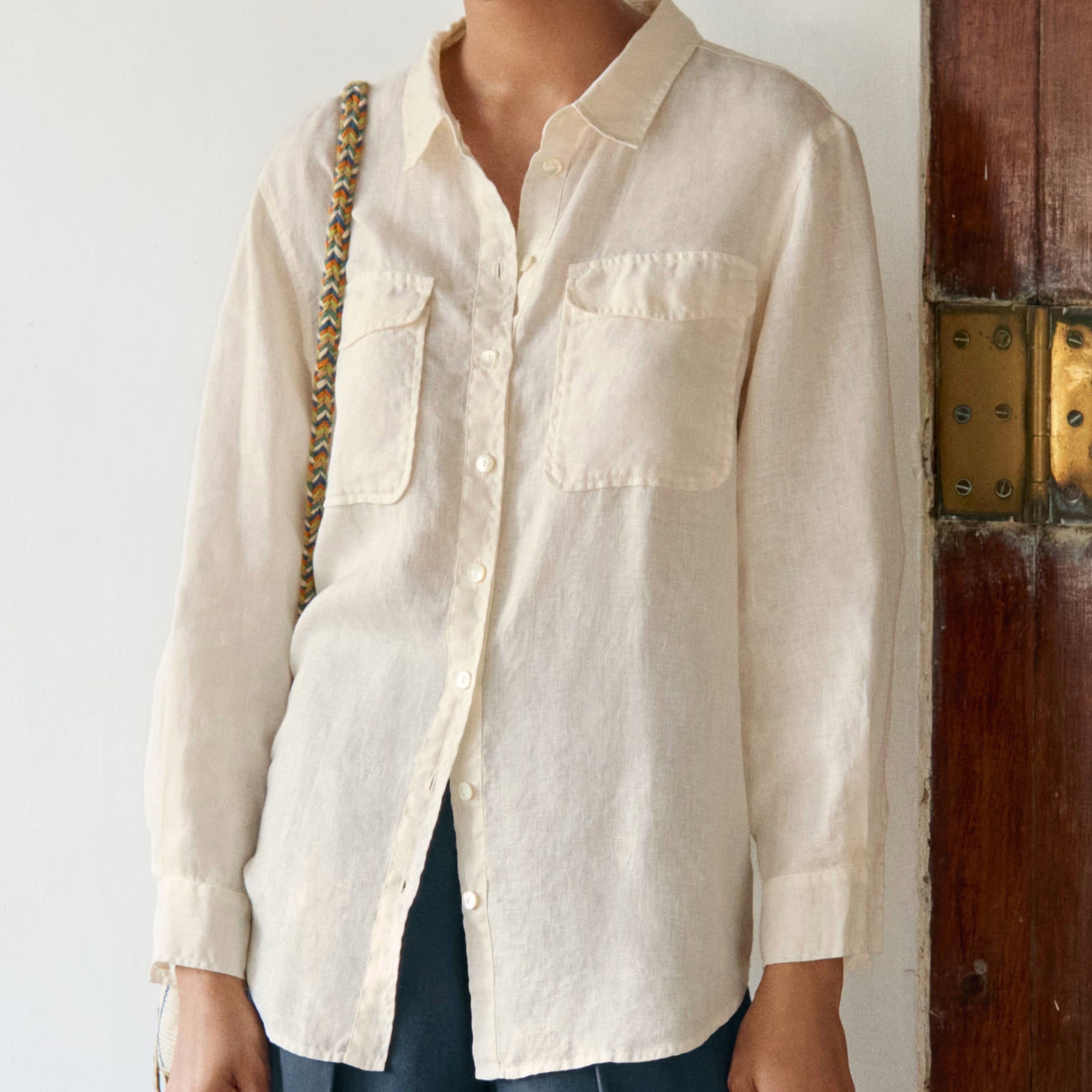 Woman wearing a beige shirt and blue pants standing against a white wall.