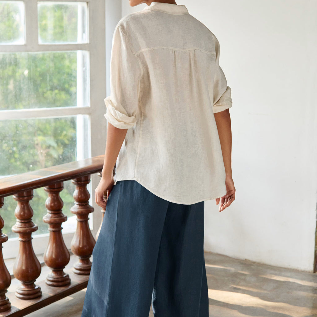 Woman wearing a white shirt and blue pants standing in a room with large windows.