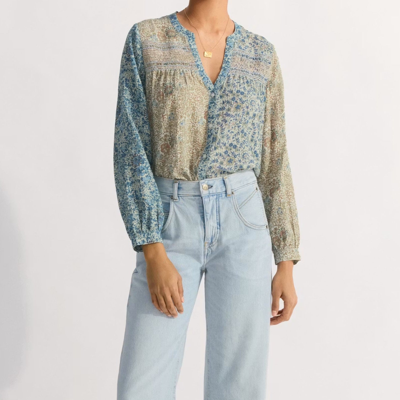 Woman wearing a patterned blouse and light blue jeans on a white background